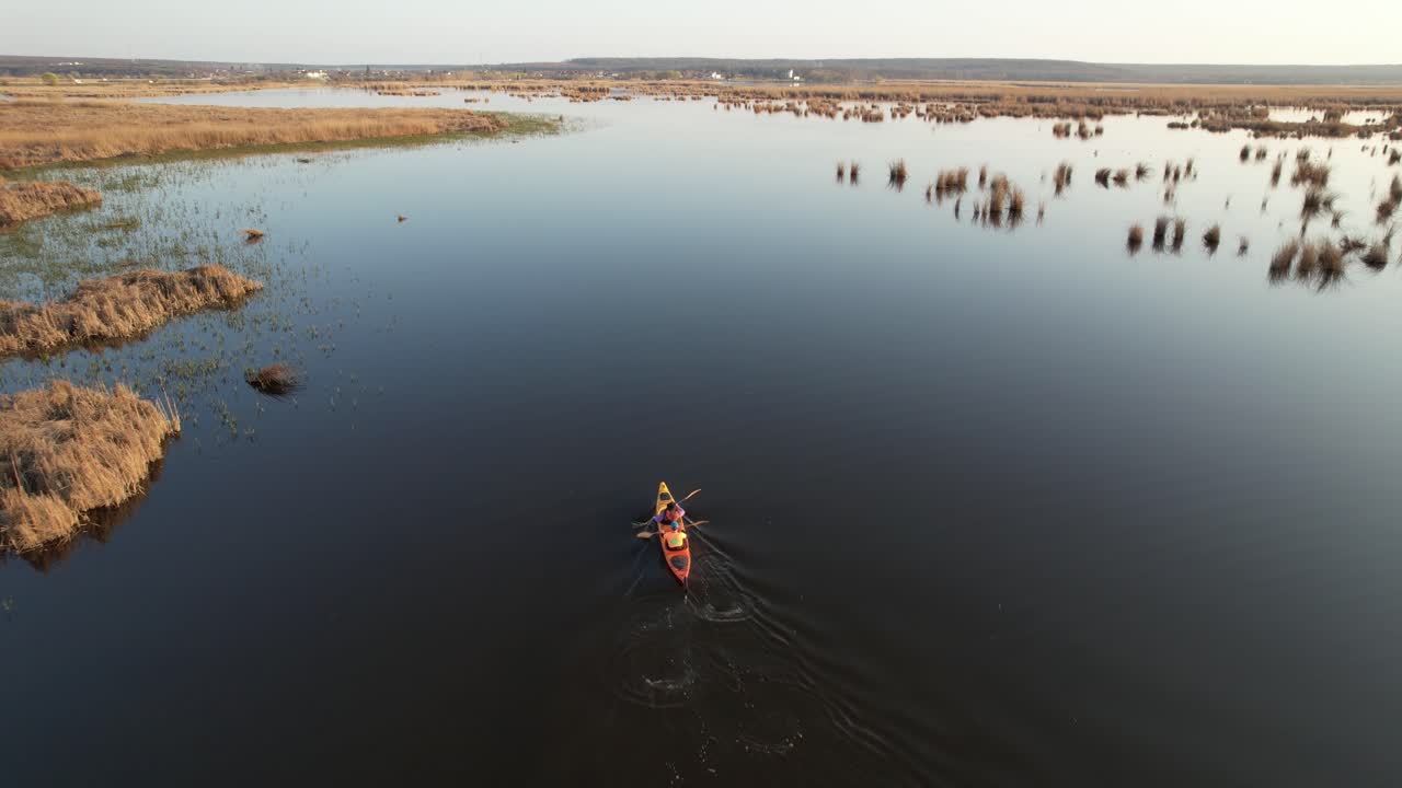 dos personas en kayak en un lago sereno rodeado de cañas y un vasto paisaje al atardecer