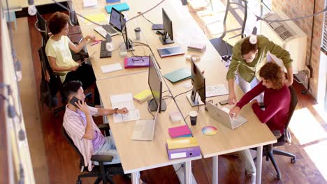 High-angle-of-diverse-female-and-male-creative-colleagues-at-work-in-casual-office,-slow-motion