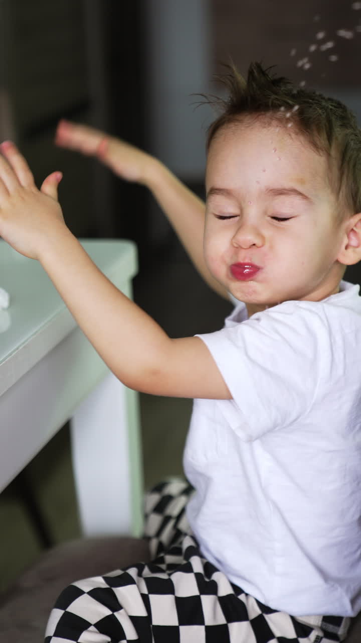 Funny kid holding water in mouth taps by the chair. Child spills the water and looks around. Vertical video.