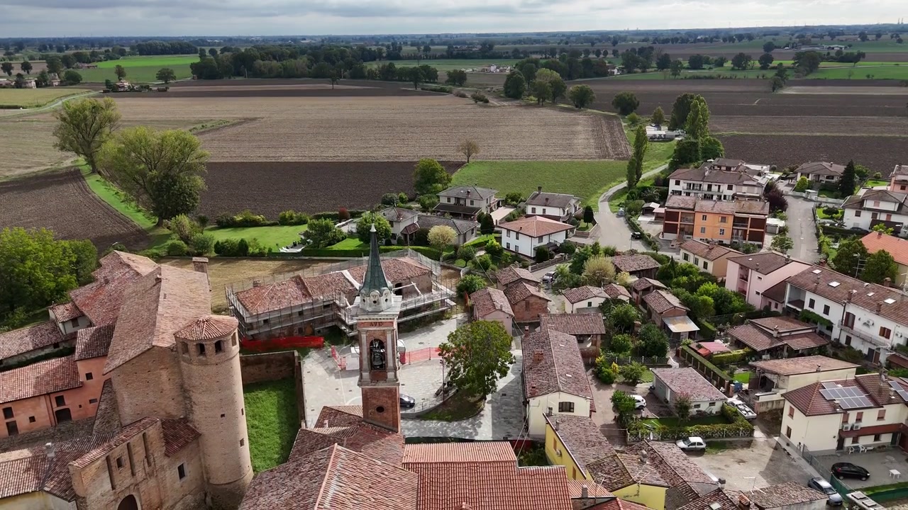 Calendasco, Piacenza, Emilia Romagna, Italia con campanile della chiesa parrocchiale, edifici storici e campi agricoli circostanti nella Pianura Padana, ripresa in discesa con drone