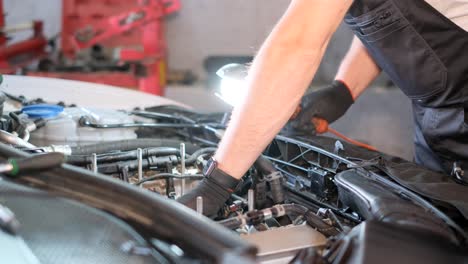 mechanic working on a car engine with a flashlight in a garage