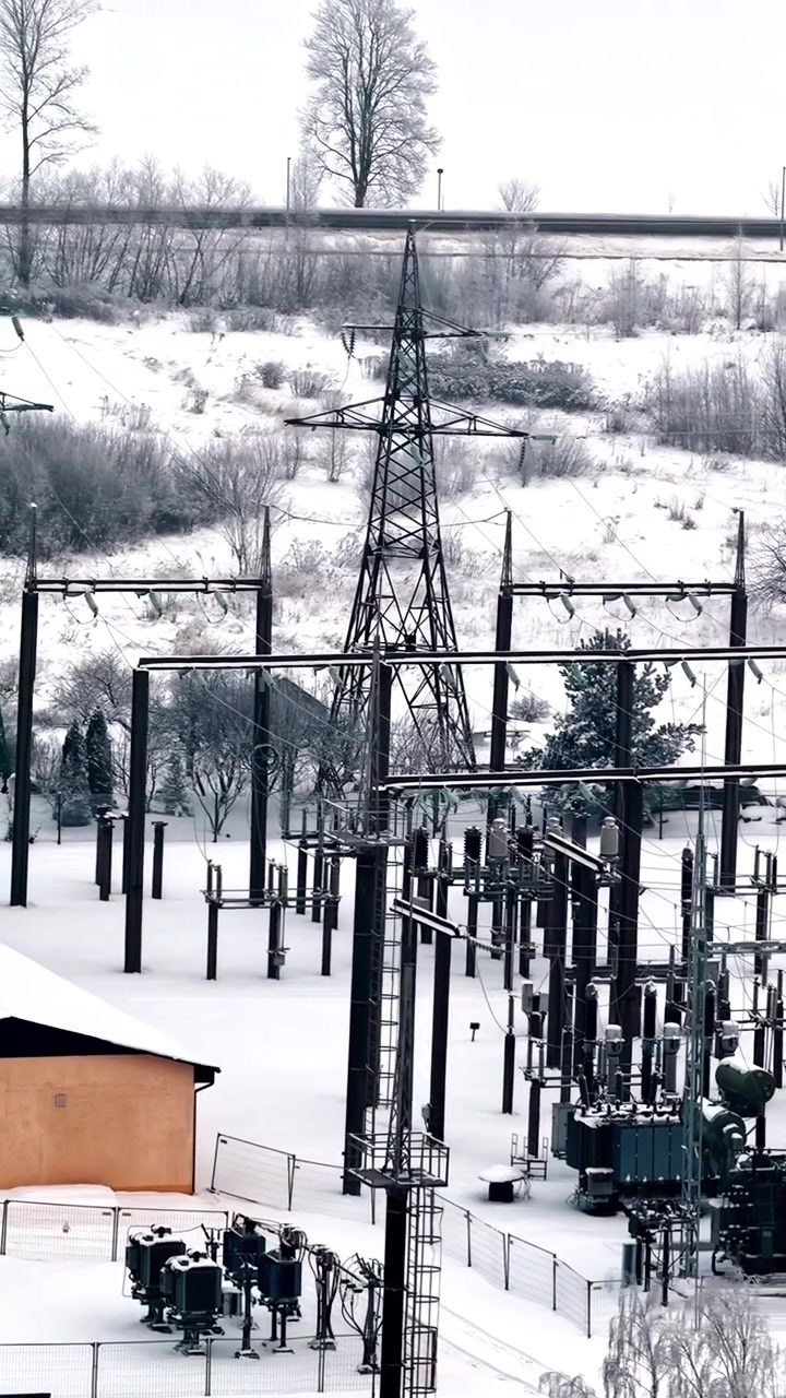 Schneebedecktes Umspannwerk mit Stromleitungen in einer ruhigen Winterlandschaft.