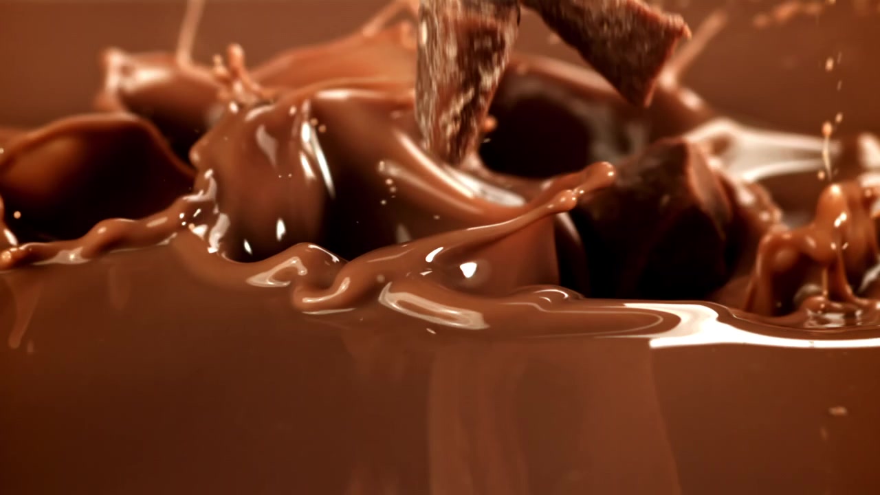 Pezzi di cioccolato che si tuffano al rallentatore nel cioccolato fuso