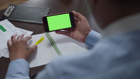 hombre afroamericano irreconocible sosteniendo un teléfono inteligente con pantalla verde chromakey pensando. joven empresario pensativo analizando el negocio de planificación de mercado electrónico en la oficina en casa en el bloqueo.