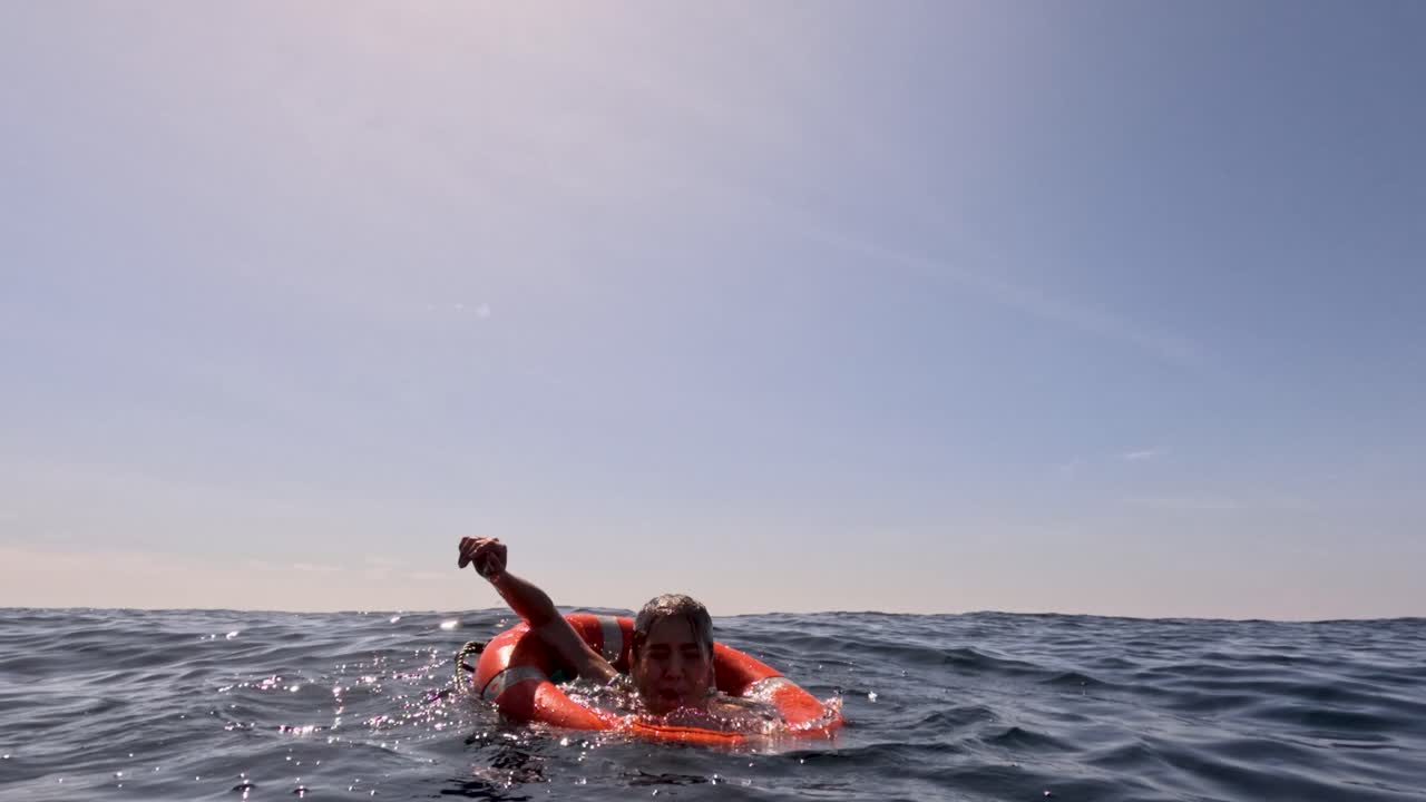 Individual struggling in ocean, grabs lifebuoy, daylight, wide shot, calm sea, underwater perspective