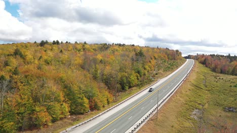 Vista-Aérea-De-Un-Coche-Solitario-En-La-Autopista-En-El-Colorido-Paisaje-Otoñal-Americano