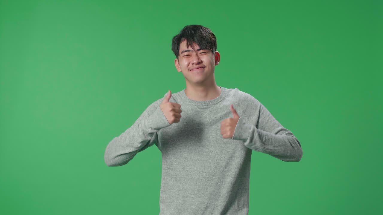 An Asian Man Showing Thumbs Up Gesture And Smiling While Standing In The Green Screen Studio