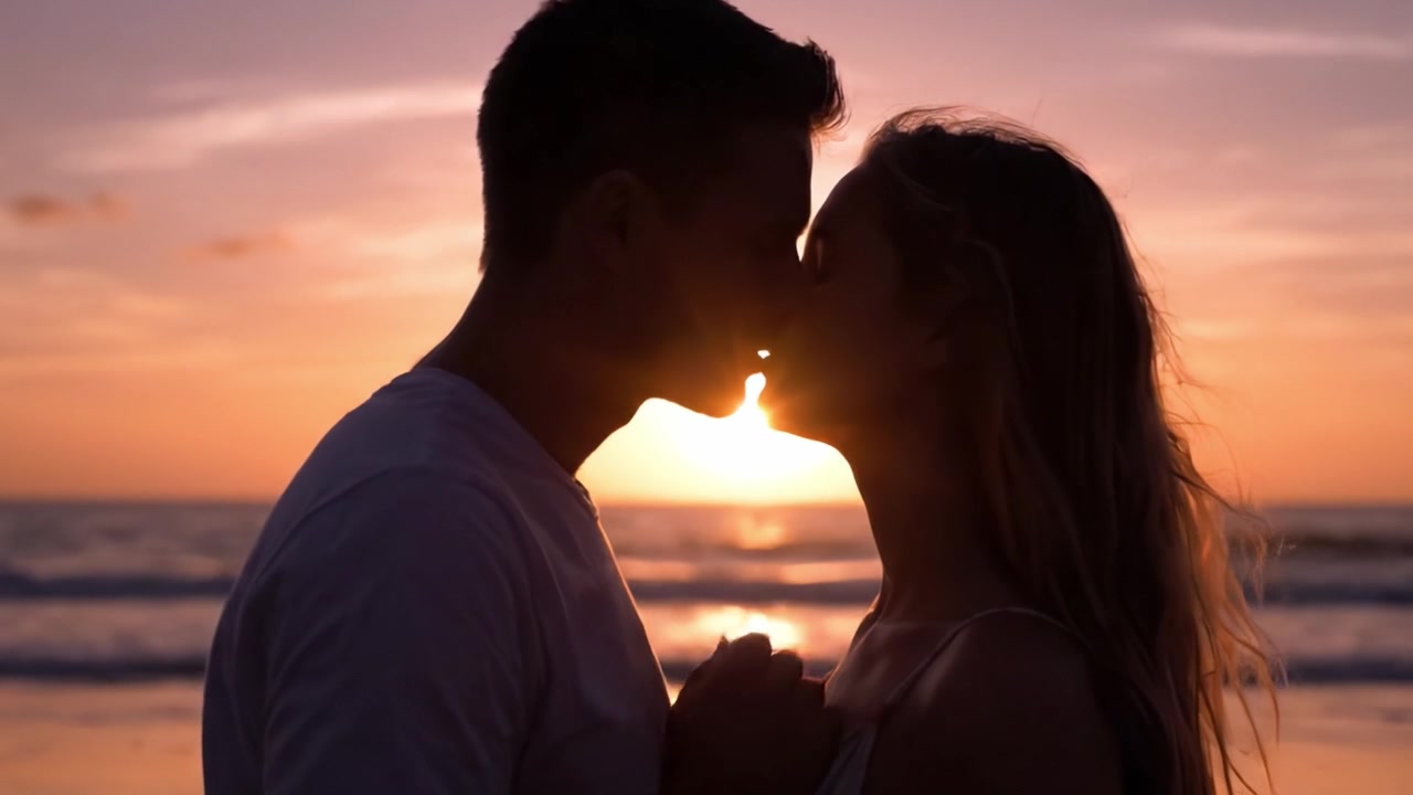 Abbraccio romantico al tramonto: una coppia celebra il proprio amore in mezzo a un tramonto mozzafiato sul mare, condividendo un bacio intimo e una silhouette contro lo splendore della natura.