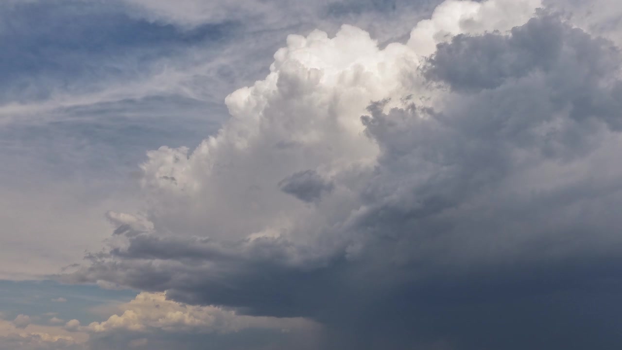 4K aerial timelapse detailing a massive monsoon storm cloud forming in the American Southwest. A bright, billowing white cumulus top contrasts against a dark, heavy underbelly and blue sky.