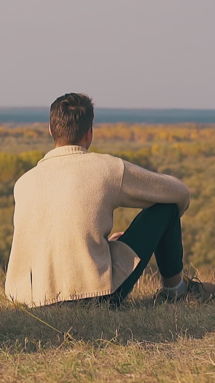 lonely guy in brown pullover sits by blue tent shadow and admires pictorial autumn forests slow motion backside view