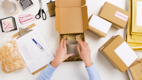 Woman-Packing-Mug-To-Parcel-Box-at-Post-Office-9.delivery,-mail-service,-people-and-shipment-concept-woman-wrapping-mug-into-protective-bubble-wrap-and-packing-it-to-parcel-box,-then-crossing-item-off-form-on-clipboard-at-post-office