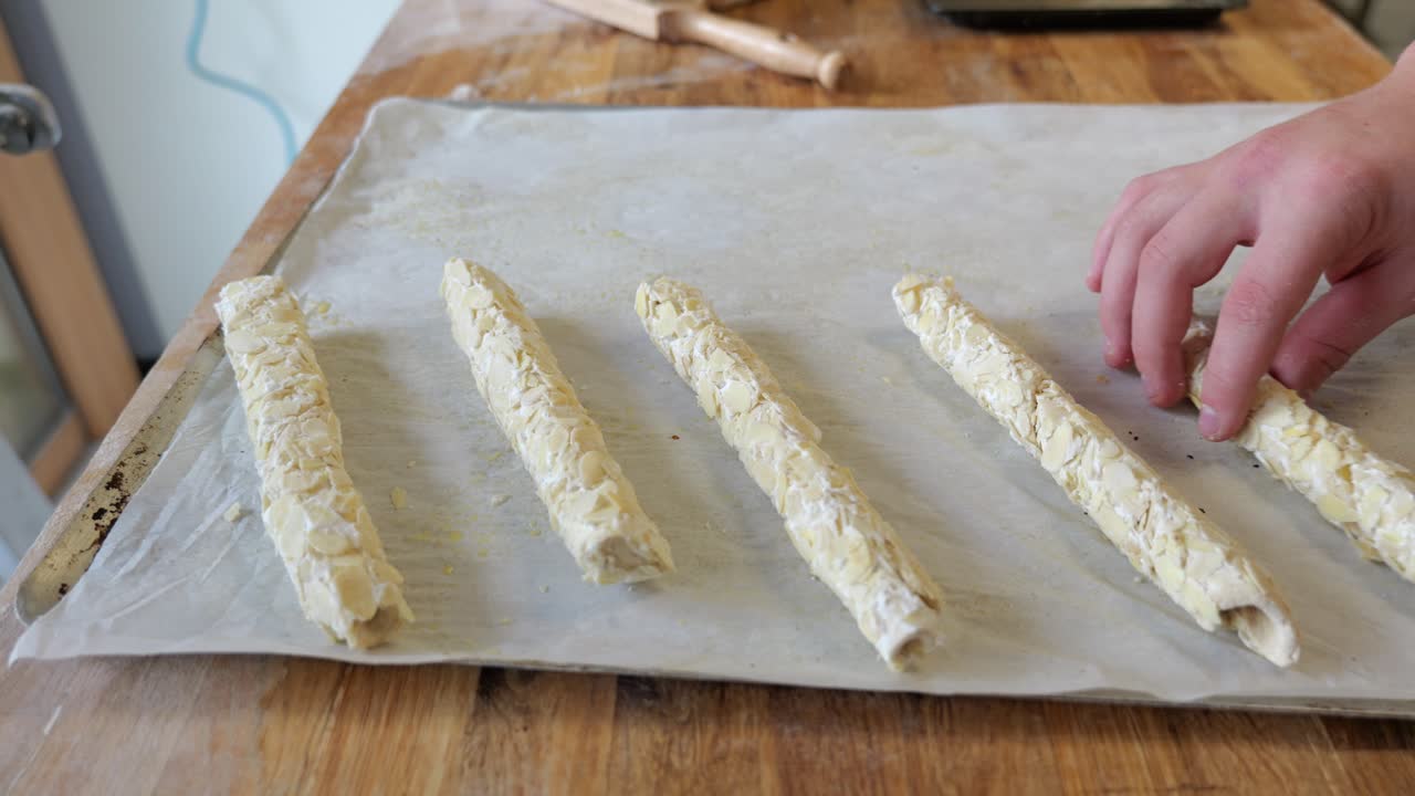 Primo piano di rotoli di pasta alle mandorle disposti su carta forno in un laboratorio di pasticceria francese prima della cottura.