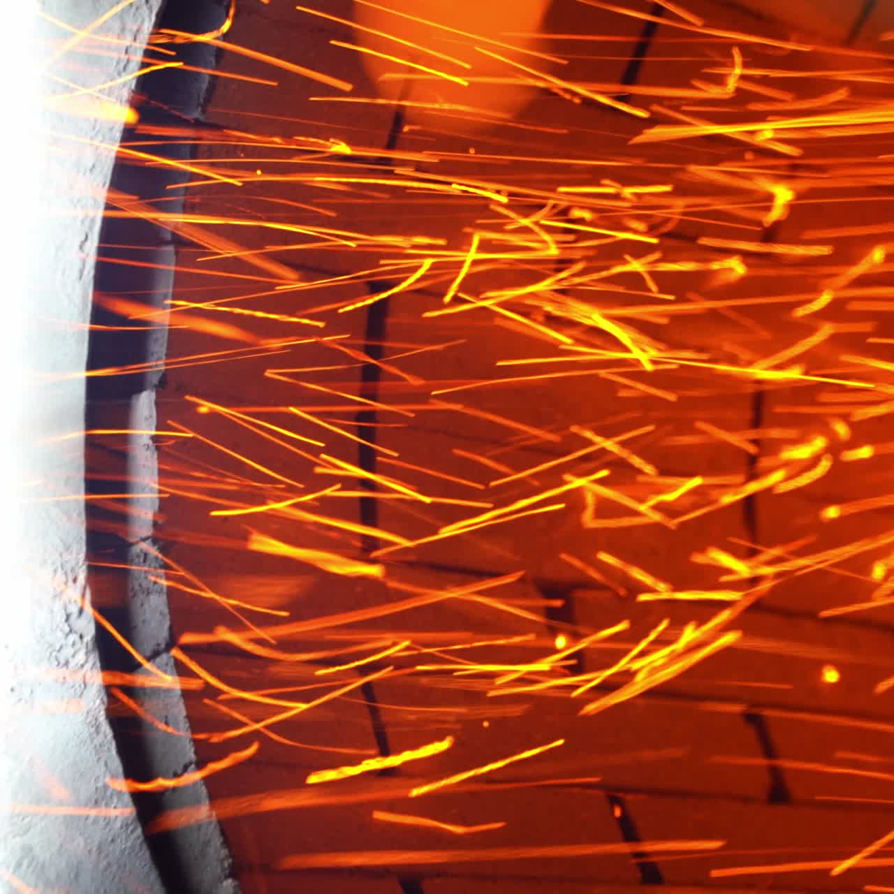Little orange sparkles flying quickly from a stove pipe. Hot red particles at the backdrop of orange bricks. Close up
