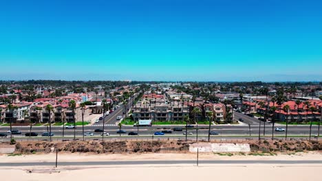 Drone-view-of-Pacific-Coast-Highway-with-some-cars,-houses,-and-people-walking-by-on-PCH-Huntington-Beach-California