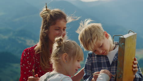 smiling family creating picture outdoor. children painting with mother on easel.