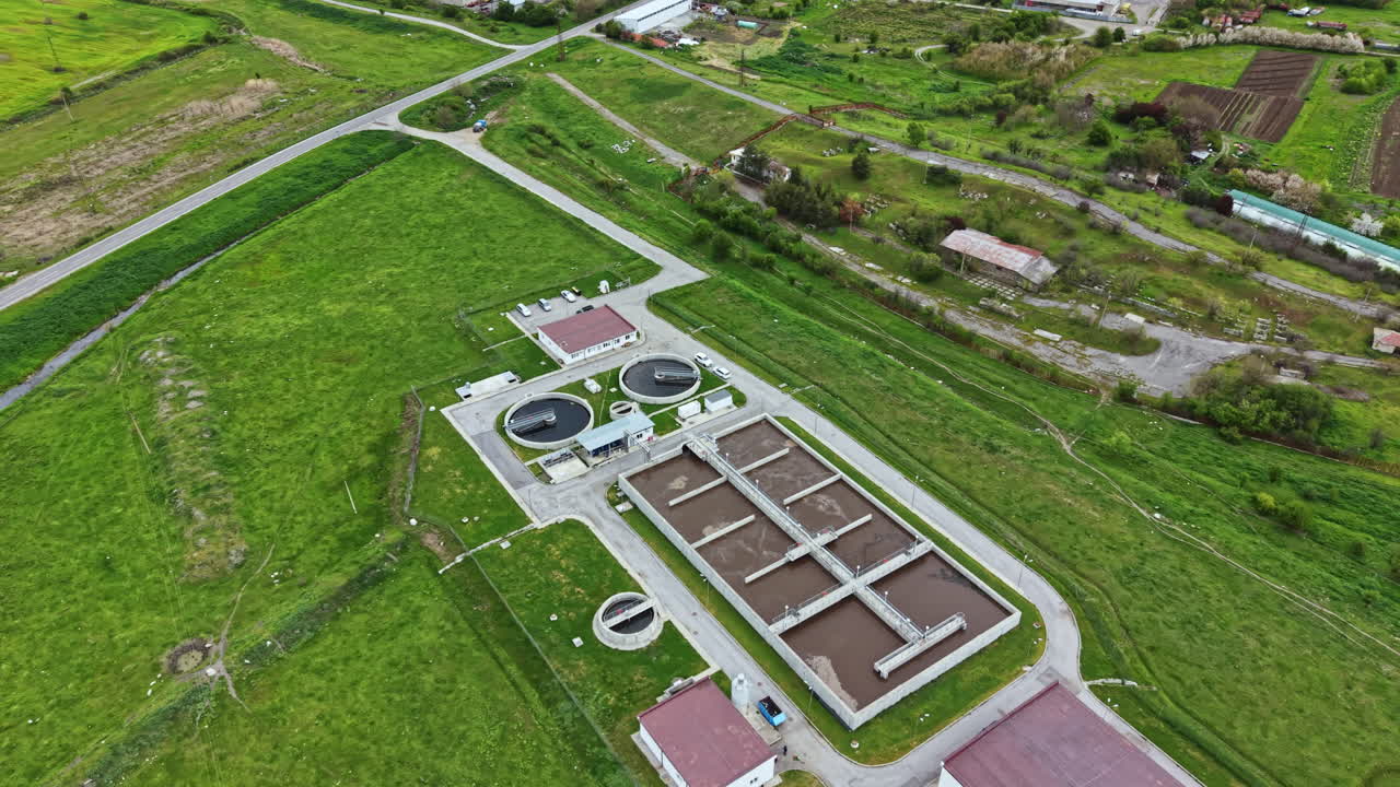 Wastewater treatment plant operates in a rural area with green fields and agricultural land nearby during a clear day