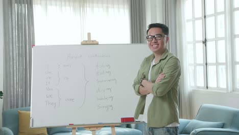asian male teacher with glasses crossing arms and smiling to camera while teaching english at home