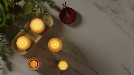 overhead view looking down on still life of lit candles and incense stick with green plant as part of relaxing spa day decor