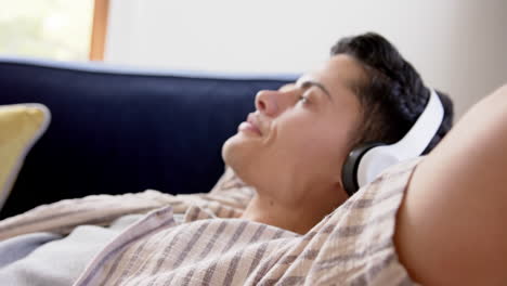 Hombre-Birracial-Feliz-Con-Auriculares-Tumbado-En-El-Sofá,-Sonriendo-Con-Los-Ojos-Cerrados,-Cámara-Lenta