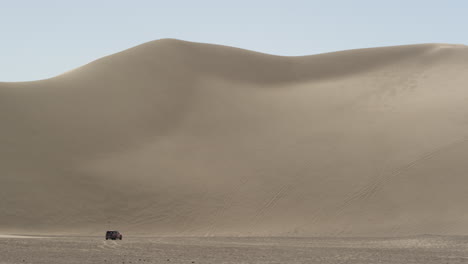 dumont dunes tower over a 4x4 truck in the nevada sun, wide and windy