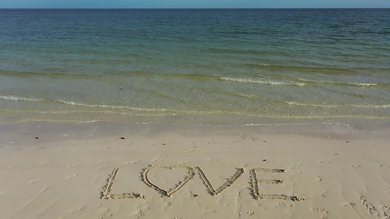 지평선에 에메랄드와 푸른 물이 있는 모래에 새겨진 사랑의 광각 사진