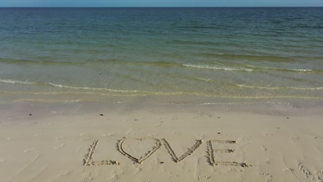 wide angle shot of love inscribed in the sand with emerald and blue water on the horizon