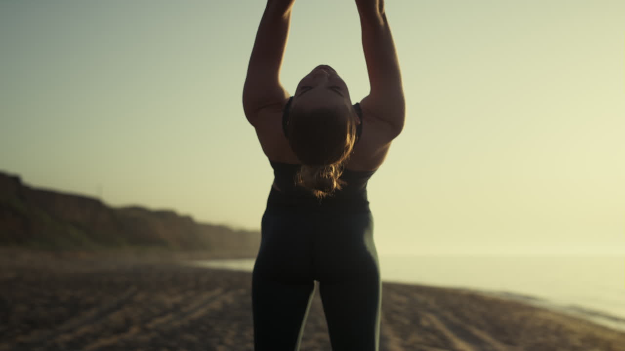 chica atractiva tirando de los brazos hacia atrás practicando la postura de puente en la puesta de sol de cerca.