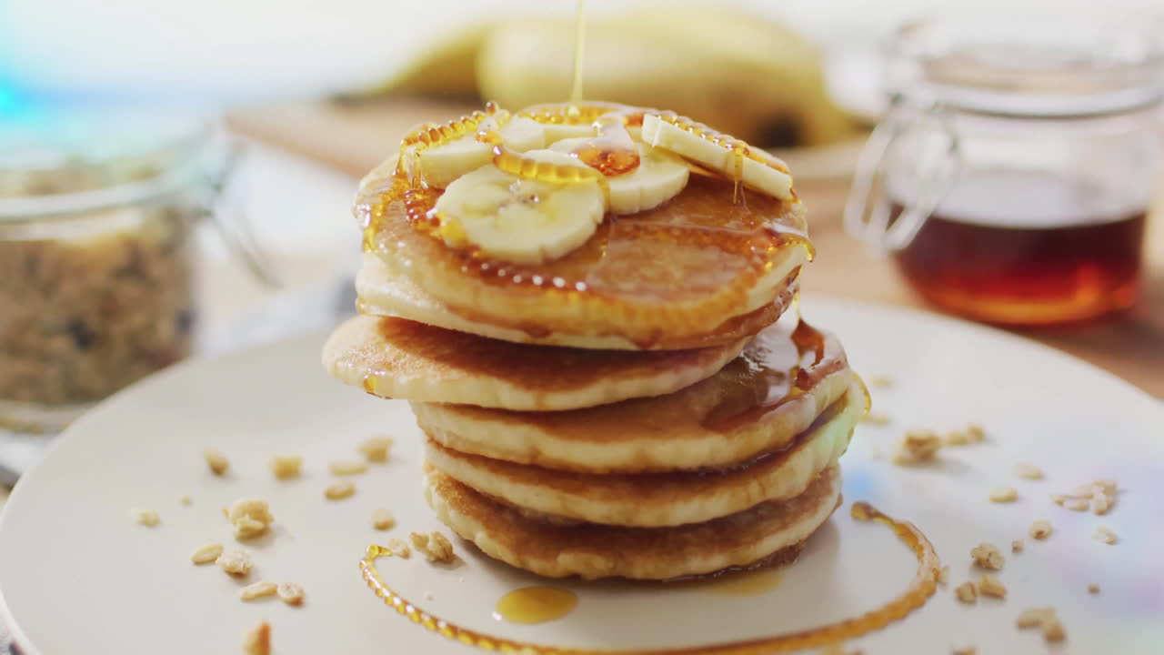 Banana slices topping pancakes with syrup on white plate in kitchen