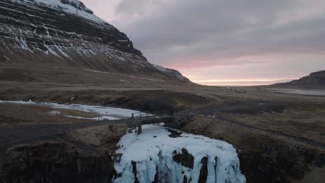 toma de drone de un hombre caminando sobre un puente sobre un río glacial y una cascada en el paisaje de islandia en un frío día de primavera