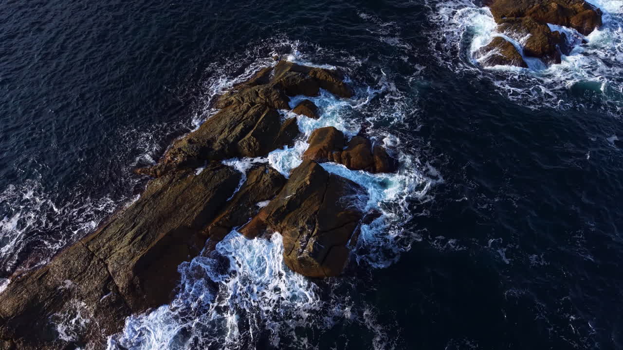 La costa rocciosa e frastagliata incontra le onde danzanti sotto il sole splendente in un sereno pomeriggio sul litorale.