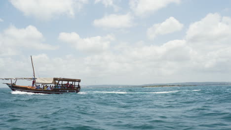 wooden dhow boat with passengers cruising on sea waves, zanzibar