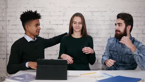 equipo de negocios multiétnico diverso abrazándose mientras están sentados a la mesa en una oficina moderna. disparo en cámara lenta