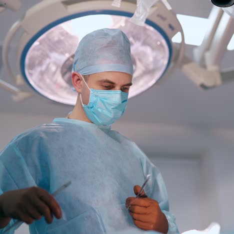 surgeon finishes the operation. doctor and a female nurse in blue masks conduct a surgery under bright medical lamp. specialists in surgical room.