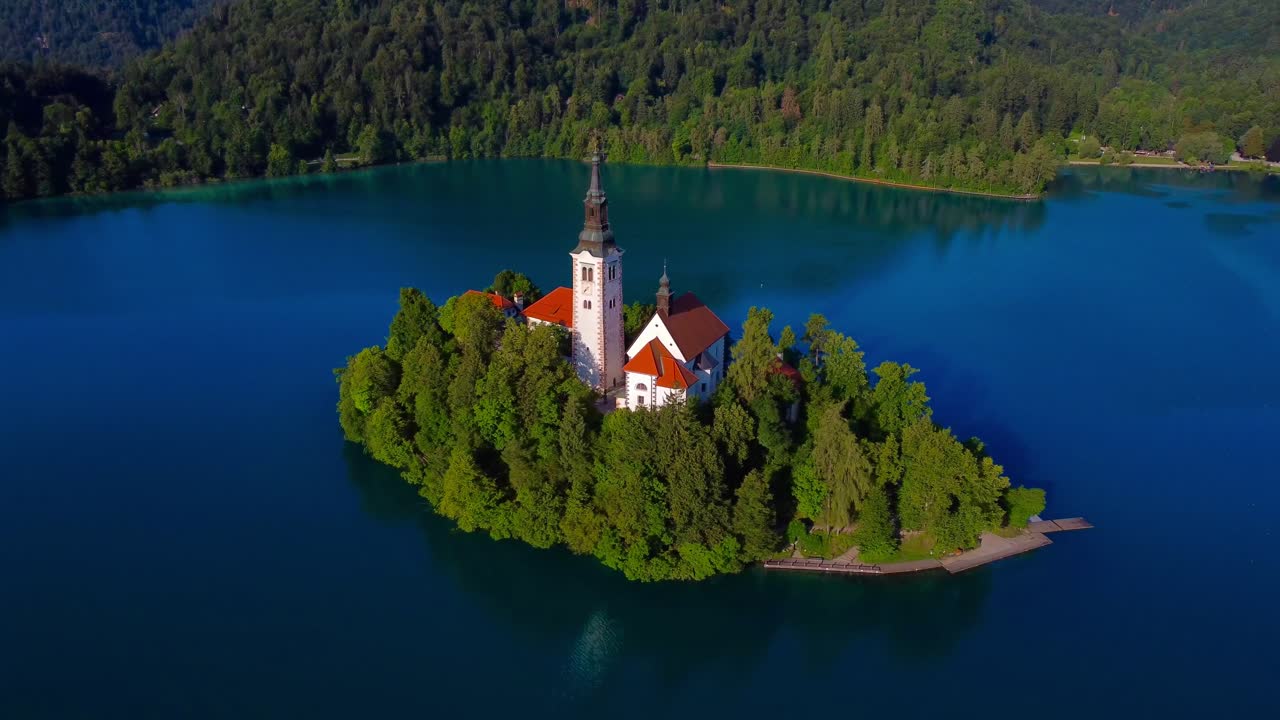 Drone che sorvola l'iconica Isola di Bled e la Chiesa dell'Assunzione della Beata Vergine Maria in una tranquilla mattina presto e soleggiata - Slovenia
