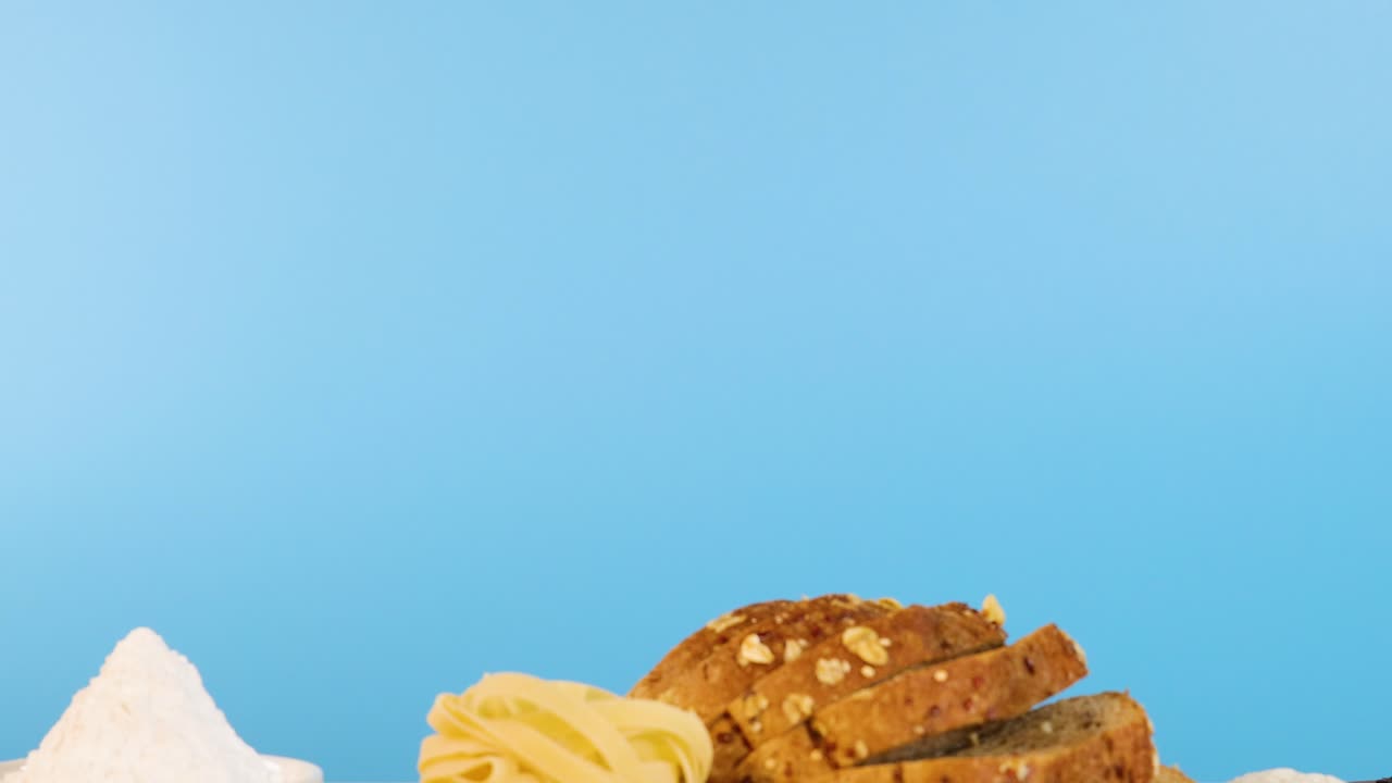 Various grains, pasta, and bread slices arranged on a table with a bright blue backdrop, highlighting diverse food textures