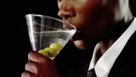 androgynous man drinking cocktail against black background