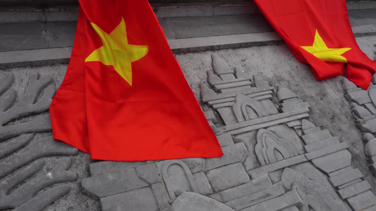 A close-up view of Vietnamese flags draping over a stone carving featuring historic architectural details of ancient Cham Temples, symbolizing national identity and cultural heritage, Fansipan Vietnam