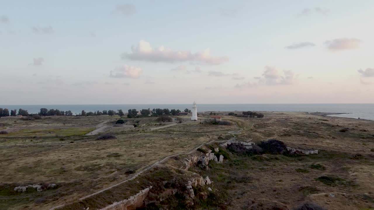 Un meraviglioso paesaggio costiero mette in mostra rovine storiche e un faro durante il tramonto. Colori tenui riempiono il cielo mentre le onde lambiscono dolcemente la riva, creando un'atmosfera tranquilla