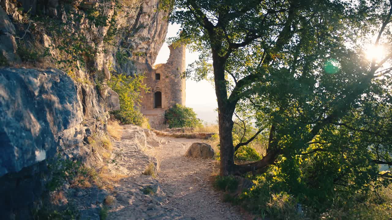 Sentiero soleggiato a picco sulla scogliera ad Autoir, in Francia, che conduce alle rovine medievali dello Château des Anglais. Parete rocciosa calcarea e alberi verdi con un bagliore di sole nella regione del Lot