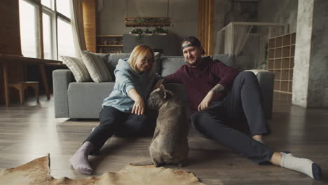 couple sitting on the floor leaning on the sofa caressing their bulldog dog 2