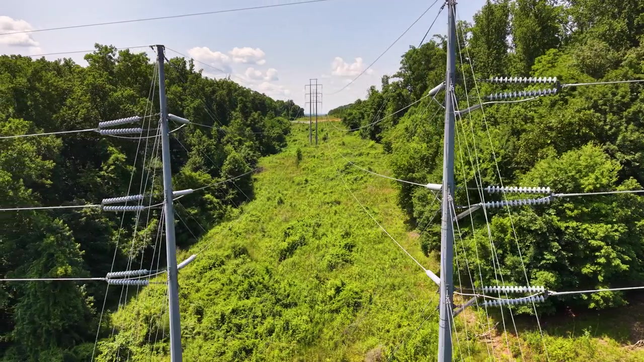 High-voltage transmission corridor near Chattanooga, Tennessee, United States, revealing steel monopoles, overhead conductors, cleared utility easement and deciduous woodland, drone slide.