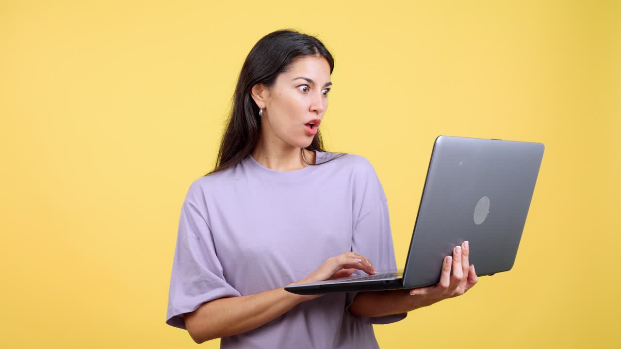 Surprised woman using a laptop on a yellow background