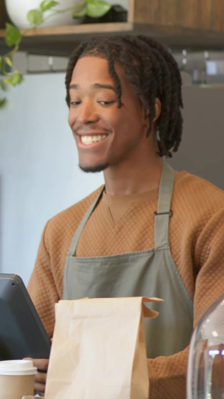 Vertical video: Customer calling, barista in apron leaning at counter checking order with bag