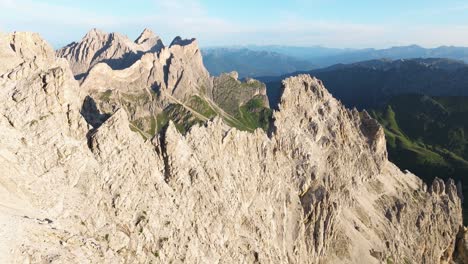 Aerial-panorama-of-the-striking-Furchetta-peak-amidst-the-Dolomites,-displaying-its-intricate-rock-formations-and-surrounding-green-valleys-bathed-in-soft-sunlight