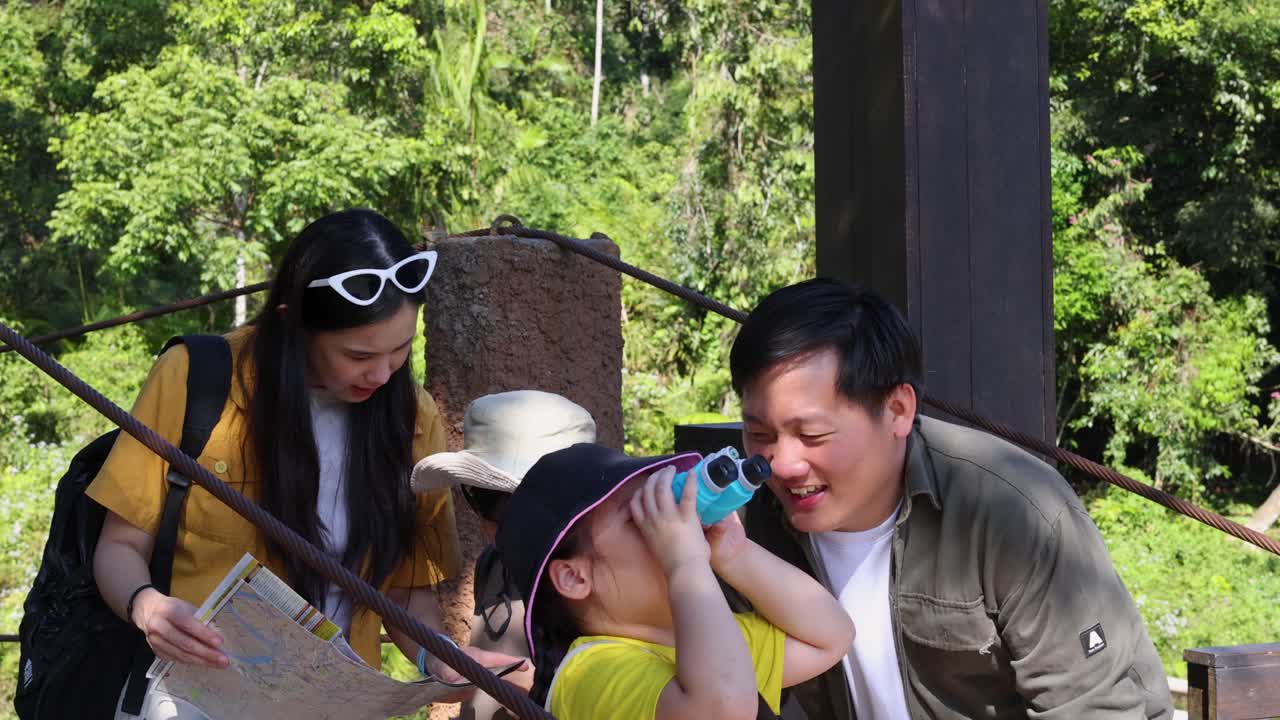 พ่อลูกชาวไทยส่องกล้องสองตาขณะชมทิวทัศน์ในสภาพแวดล้อมป่าที่เขียวชอุ่ม