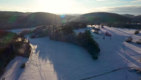 Increíble-Panorámica-Aérea-A-Través-De-Montañas-Cubiertas-De-Nieve,-Bosques-Y-Cielo-Claro-Y-Soleado-Durante-El-Invierno-En-Suabia,-Alemania