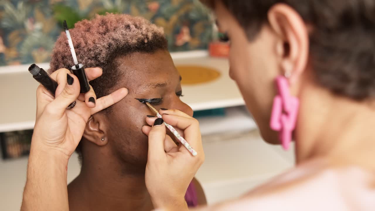 African transgender man with his eyes closed as a colleague applies make-up