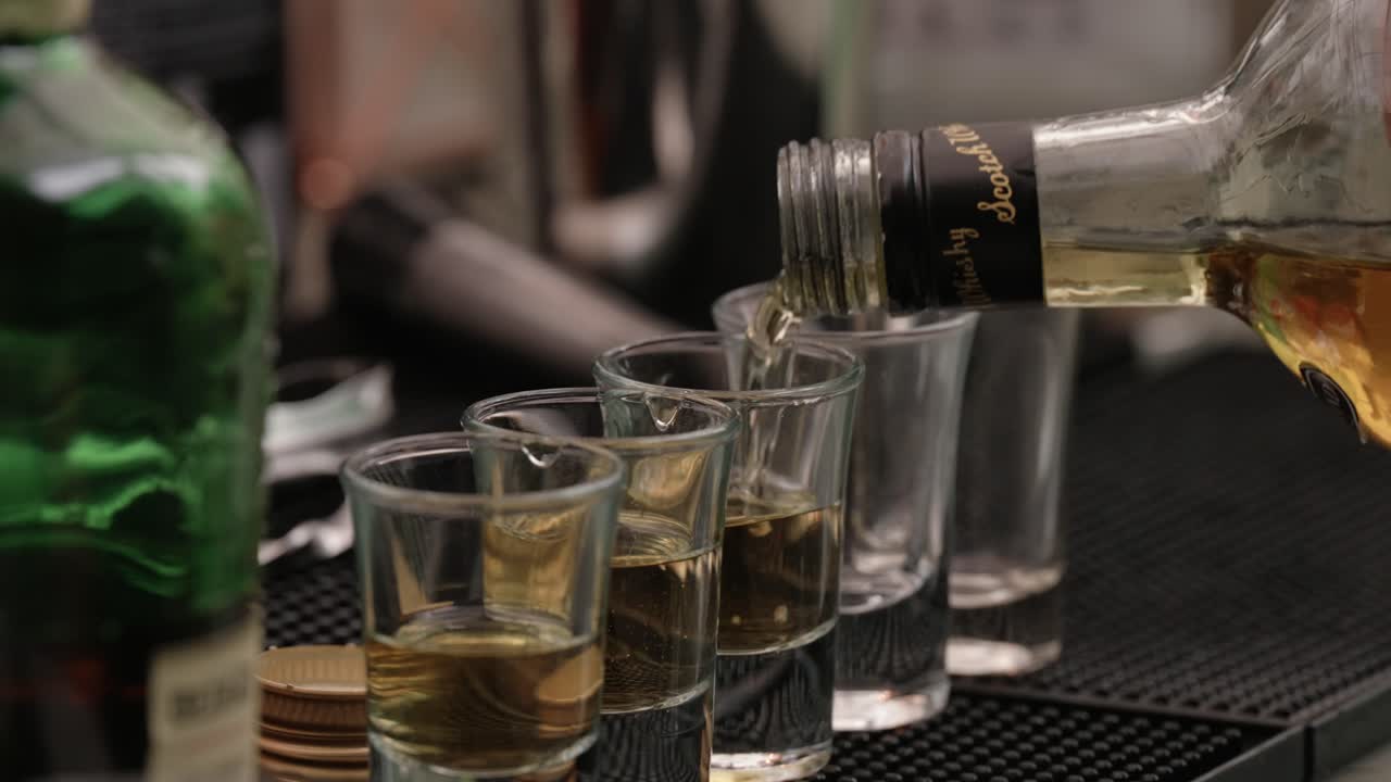 Close up of whiskey being poured into shot glasses at a bar counter