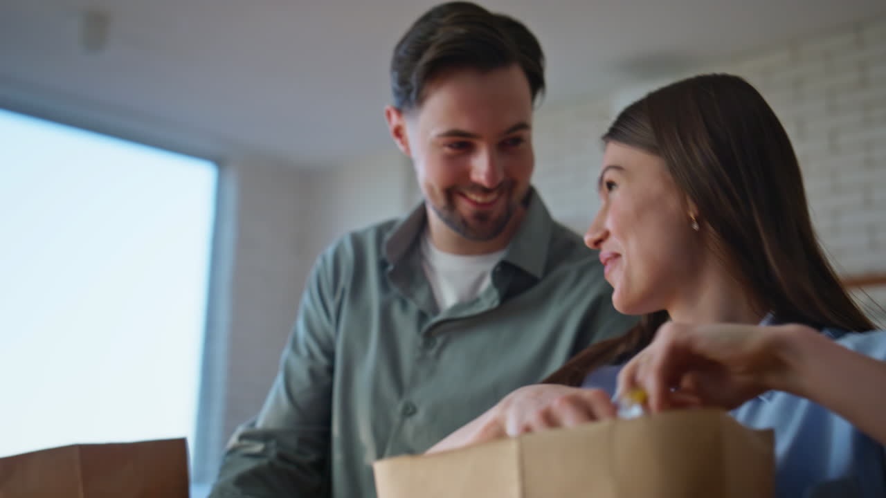 Home pair carrying groceries in paper bags stepping kitchen interior closeup