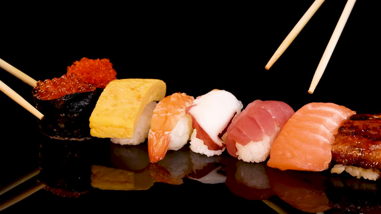 Le bacchette selezionano un pezzo di nigiri di tonno da un assortimento di sushi ben disposto su una superficie nera lucida sotto un'illuminazione brillante e uniforme